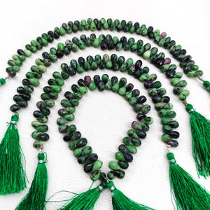 May include: Three strands of green gemstone beads with a teardrop shape. The beads have black and pink flecks. Each strand has a green tassel at the end.