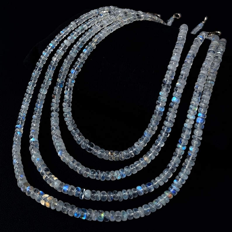 Puede incluir: Cinco hilos de collares de piedras preciosas claras e iridiscentes. Las cuentas son peque&ntilde;as y redondas, con destellos de azul y blanco. Los collares se exhiben sobre un fondo negro, mostrando los delicados detalles de la joyer&iacute;a.