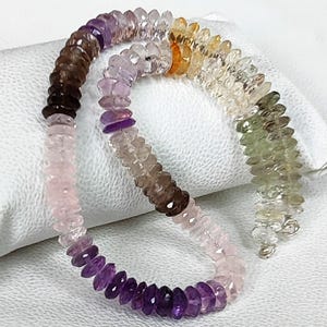 Könnte beinhalten: Eine mehrfarbige Edelsteinkette mit facettierten Rondellperlen in einem Farbverlauf aus Violett, Braun, Rosa, Transparent, Gelb und Grün. Die Perlen sind auf einem durchgehenden Strang aufgereiht und zeigen eine Vielfalt an Tönen.
