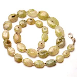 May include: A necklace featuring oval-shaped, light green gemstones with silver-colored beads and a clasp. The stones have a natural, organic appearance with variations in color and texture, creating a unique jewelry piece.