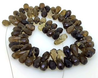 May include: A strand of brown and clear faceted teardrop-shaped gemstone beads. The beads are strung on a thin wire and are arranged in a circle.