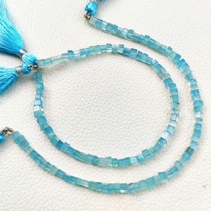 Puede incluir: Una hebra de cuentas cuadradas de color azul claro con un borla en cada extremo. Las cuentas están enhebradas en un hilo transparente.