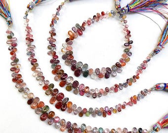 May include: Strands of colorful gemstone beads in various shades of red, pink, purple, and green. Each strand is adorned with a tassel of multicolored threads. The beads are teardrop-shaped and strung together.