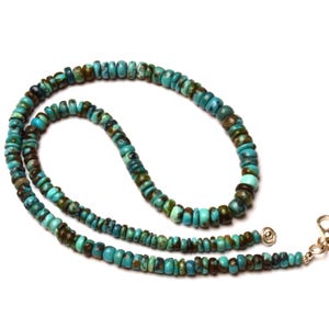 May include: A turquoise beaded necklace with a silver clasp. The necklace features small, round beads in shades of turquoise and brown. The beads are strung together to form a long, elegant necklace.