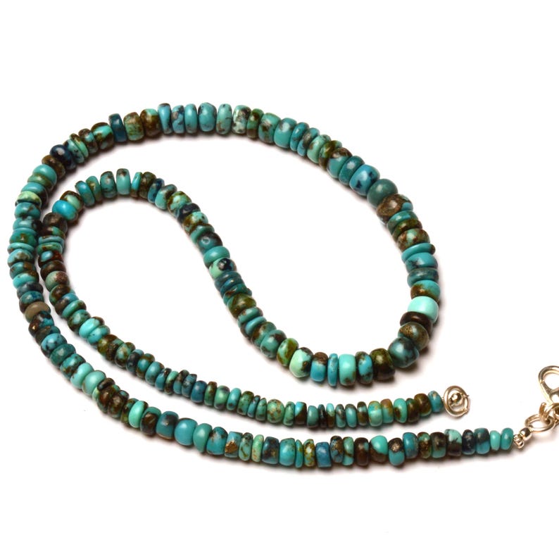 May include: A turquoise beaded necklace with a silver clasp. The necklace features small, round beads in shades of turquoise and brown. The beads are strung together to form a long, elegant necklace.