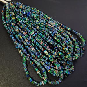 Puede incluir: Una hebra de chips de piedras preciosas azules, verdes y negras. Las chips son de forma irregular y tienen un acabado brillante e iridiscente.