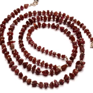 May include: A long necklace made of small, irregular, red ruby beads. The necklace is strung on a thin gold chain.