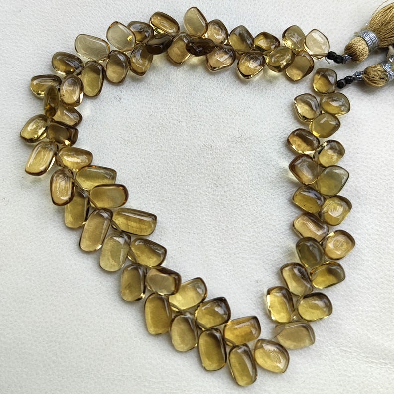 May include: A necklace composed of numerous, irregularly shaped, amber-colored gemstones. The stones are strung together, forming a curved shape. The necklace has a tassel at the end, with silver-colored accents and black beads.