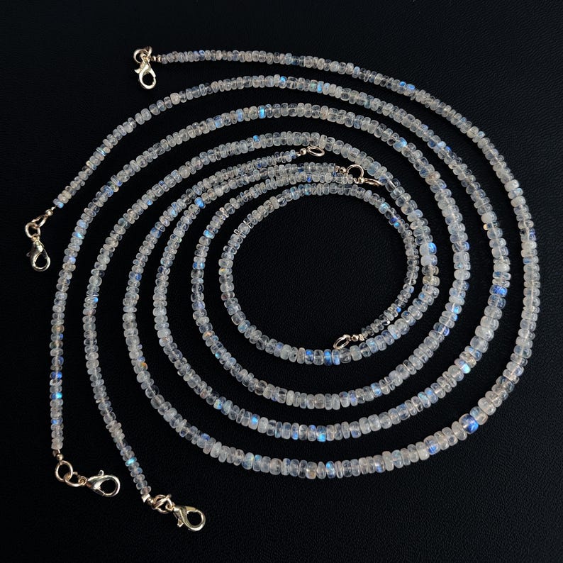 Puede incluir: M&uacute;ltiples hilos de delicados collares de cuentas con un aspecto brillante e iridiscente. Las peque&ntilde;as cuentas redondas son de un color p&aacute;lido y transl&uacute;cido con destellos azules. Cada collar est&aacute; terminado con un cierre plateado.