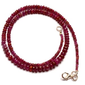May include: A necklace composed of small, round, deep red ruby beads. The beads are strung together, creating a layered effect. The necklace has a gold-colored clasp and a delicate design, suitable for various occasions.