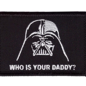May include: Black rectangular patch featuring an embroidered image of Darth Vader's helmet in white. The text "WHO IS YOUR DADDY?" is embroidered below the image in white.