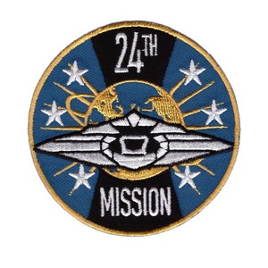 May include: Circular embroidered patch with a blue background, white stars, and gold detailing. The text "24TH MISSION" is displayed in white. The patch has a gold border.