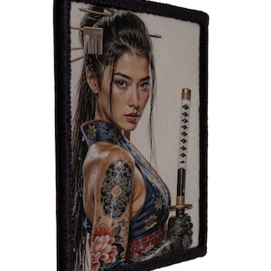 Könnte beinhalten: Rechteckiger Aufnäher mit einem Porträt einer Frau mit langen dunklen Haaren, die ein Katana hält. Sie hat ein Blumen-Tattoo auf dem Arm und trägt ein blaues und rotes Outfit. Der Aufnäher hat einen schwarzen Rand.