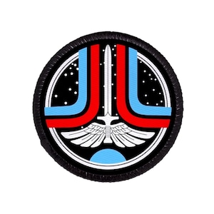 Op de afbeelding: Ronde patch met een zwarte rand. Het ontwerp toont een wit zwaard, vleugels en een blauw-rode boog. De achtergrond is zwart met witte stippen en een blauwe halve cirkel aan de onderkant. Geschikt voor kleding of accessoires.