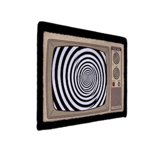 Op de afbeelding: Een vloerkleed in de vorm van een retro televisie. Het scherm toont een zwart-wit spiraalpatroon. Het vloerkleed heeft een beige frame met zwarte rand en twee knoppen aan de rechterkant.