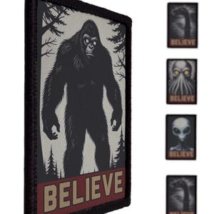 Pode incluir: Patch em preto e branco com uma ilustração de Bigfoot em um cenário de floresta. A palavra "BELIEVE" é exibida em uma faixa vermelha e bege na parte inferior. Patches adicionais com designs de criptídeos e alienígenas também são visíveis.