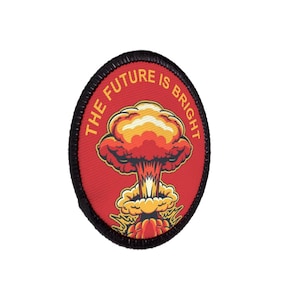 Könnte beinhalten: Ovaler Aufnäher mit rotem Hintergrund und schwarzem Rand. Der Aufnäher zeigt eine stilisierte Atompilz-Grafik in Gelb-, Orange- und Rottönen. Der Text "THE FUTURE IS BRIGHT" ist am oberen Rand angeordnet.