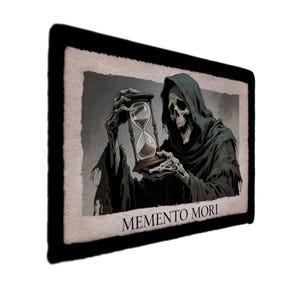以下が含まれることがあります： 黒い縁取りの長方形パッチには、砂時計を持つ死神が描かれています。死神は、暗いマントと骸骨の顔で描かれています。「Memento Mori」というフレーズが画像の下部に印刷されています。