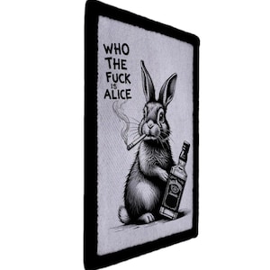 Op de afbeelding: Zwart-wit patch met een konijn dat een sigaret rookt en een fles whisky vasthoudt. De tekst "WHO THE FUCK IS ALICE" staat boven het konijn gedrukt. De patch heeft een zwarte rand.