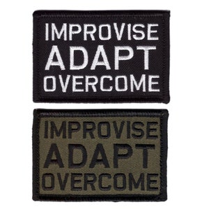 Puede incluir: Dos parches rectangulares. El parche superior es negro con texto bordado blanco que dice "IMPROVISE ADAPT OVERCOME". El parche inferior es verde oliva con texto bordado negro que dice "IMPROVISE ADAPT OVERCOME".