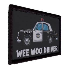 May include: Black rectangular patch with a black border. The patch features a cartoon police car with the word "POLICE" on the side. The text "WEE WOO DRIVER" is printed in white below the car.