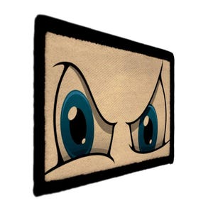 May include: A rectangular patch with a cartoon illustration of angry eyes. The eyes are blue with black outlines, set against a tan background with a black border. The design has a bold, graphic style.