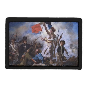 May include: A framed print of Eugène Delacroix's "Liberty Leading the People." The artwork depicts a woman holding a French flag, leading a crowd of people through a battle scene. The print is framed in black.