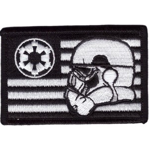 May include: A rectangular embroidered patch featuring a black and white flag design. The canton displays a circular Imperial crest, while the field shows a profile view of a white stormtrooper helmet layered over horizontal black and white stripes.