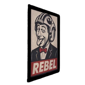 May include: A rectangular patch with a black border shows a vintage illustration of a man wearing a helmet and a bow tie, sticking out his tongue. The word "REBEL" is displayed in red block letters at the bottom.