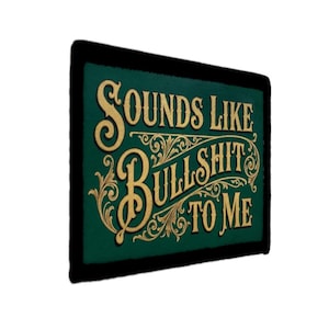 May include: A rectangular sign with a dark green background and a black border. The text "SOUNDS LIKE BULLSHIT TO ME" is written in gold, ornate lettering.