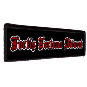 May include: A rectangular black patch with the phrase "Fortis Fortuna Adiuvat" in red script with a white outline. The patch has a black border and is set against a white background.