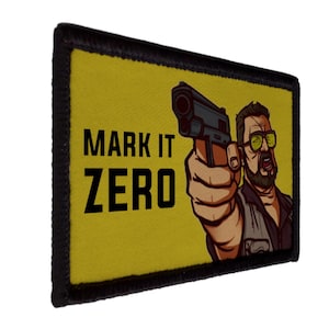 Pode incluir: Um patch retangular com fundo amarelo e borda preta. O patch apresenta o texto "MARK IT ZERO" em letras pretas em negrito. Há também uma ilustração de um homem segurando uma arma.