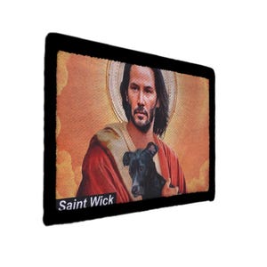 May include: Rectangular patch featuring a portrait of a man with long hair, holding a black dog, with a halo. The image is set against a textured background with the text "Saint Wick" at the bottom.