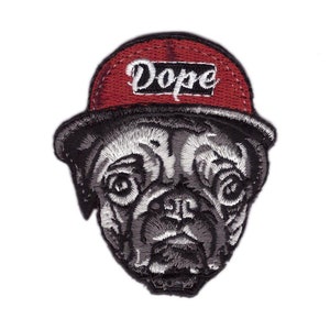 Puede incluir: Parche bordado con la imagen de un carlino con una gorra de béisbol roja. La gorra lleva la palabra "Dope" en letras blancas. La cara del carlino está detallada con tonos grises y blancos, creando una apariencia texturizada.