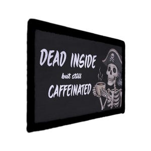 May include: Black rectangular sign with the words "DEAD INSIDE but still CAFFEINATED" in white script. A cartoon skeleton wearing a pirate hat and holding a coffee cup is on the right side of the sign.