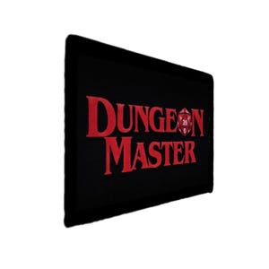 May include: Black rectangular mat with the words "DUNGEON MASTER" in red, stylized lettering. A red twenty-sided die graphic is between the words "DUNGEON" and "MASTER".