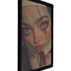 May include: A rectangular patch with a portrait of a person in a nun's habit, with striking makeup and blood-like streaks. The patch has a black border.