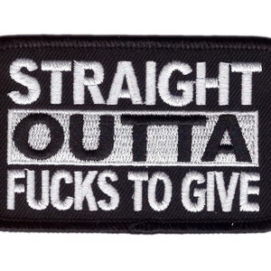Op de afbeelding: Zwart rechthoekig embleem met witte geborduurde tekst: "STRAIGHT OUTTA FUCKS TO GIVE". Het embleem heeft een zwarte rand en is bedoeld om op kleding of accessoires te naaien.