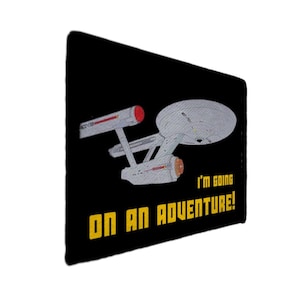 Könnte beinhalten: Schwarze rechteckige Grafik mit dem Raumschiff Enterprise aus Star Trek in Grau und Rot. Gelber Text lautet: "I'm going on an adventure!"