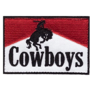 May include: Embroidered patch featuring a cowboy riding a bucking bronco. The design is set against a red and white background, with the word "Cowboys" in bold, black letters. The patch has a black border.