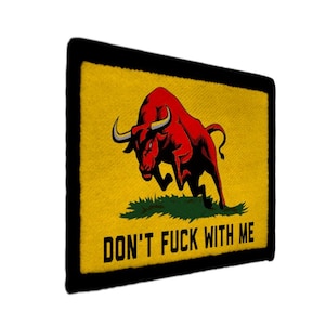 Könnte beinhalten: Ein rechteckiger Aufnäher mit schwarzem Rand und gelbem Hintergrund. Ein roter Bulle mit schwarzen Hörnern stürmt über grünes Gras. Der Text "DON'T FUCK WITH ME" ist unten in Schwarz gedruckt.