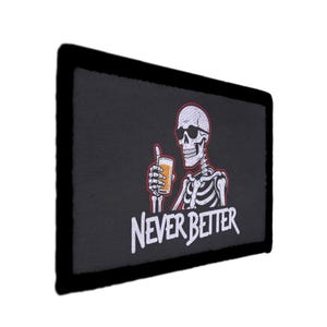 May include: Black rectangular patch with a white embroidered skeleton wearing sunglasses and holding a beer. The text "NEVER BETTER" is below the skeleton. The patch has a black border.