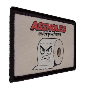 May include: Rectangular patch with a black border. It features the words "ASS HOLES" in red, above "everywhere". A cartoon toilet paper roll with an angry face is below the text. The background is off-white.