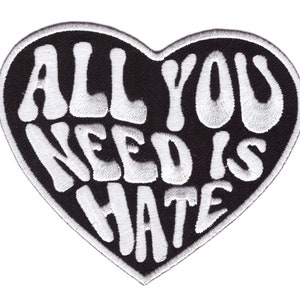 以下が含まれることがあります： 黒いハート型のワッペン。白い刺繍で「ALL YOU NEED IS HATE」と書かれています。ワッペンは黒い縁取りがあり、衣類やアクセサリーにアイロン接着または縫い付けられるように設計されています。