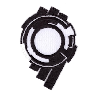 Könnte beinhalten: Ein schwarz-weiß gestickter Aufnäher mit einem kreisförmigen Design. Er zeigt einen weißen Mittelkreis, umgeben von schwarzen geometrischen Formen. Der Aufnäher eignet sich zur individuellen Gestaltung von Jacken, Taschen oder anderen Textilien.