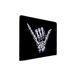May include: Black rectangular mousepad featuring a white skeletal hand in the 'hang loose' gesture. The design is a detailed illustration of the bones, creating a striking contrast against the dark background. The mousepad is likely made of a smooth material.