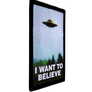 May include: Rectangular patch with a black border featuring a UFO over a forest. The text "I WANT TO BELIEVE" is printed in white block letters below the image of the flying saucer.