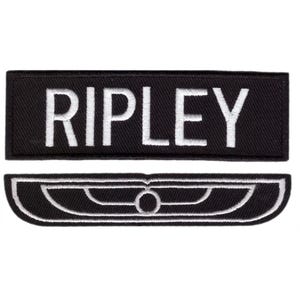 Peut inclure: Deux écussons brodés noirs. Le patch supérieur porte l'inscription "RIPLEY" en lettres majuscules blanches. Le patch inférieur est un motif blanc stylisé sur fond noir, ressemblant à une aile ou un emblème stylisé.