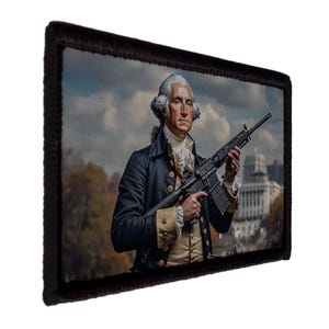 May include: A rectangular patch featuring a portrait of George Washington holding a rifle. Washington is dressed in a dark blue coat and cream-colored waistcoat. The background shows a cloudy sky and a building with a dome. The patch has a black border.