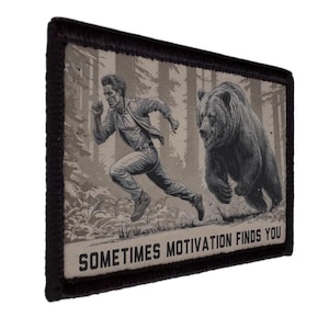 May include: A rectangular patch with a black border features a black and white illustration of a person running from a bear in a forest. The text "SOMETIMES MOTIVATION FINDS YOU" is at the bottom.